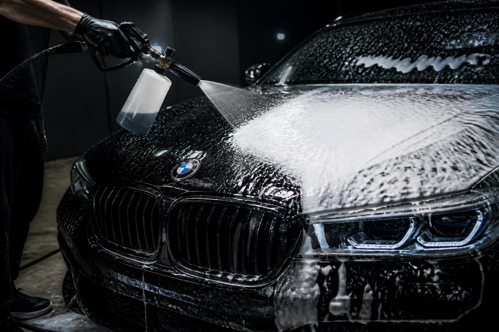 Professional detailer applying foam to a luxury black BMW